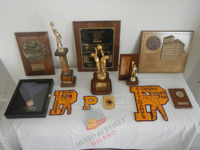 L'orgoglio e i trofei di Arturo Kenney con la sua Power Memorial Academy di New York, tutto in una foto. Allenato da Jack Dohonue e compagno di squadra di Lew Alcindor, con il suo #41 è stato campione CHSAA 1962/63 e 1963/64 senza perdere una partita, ed ha dato vita a memorabili scontri con la De Matha HS celebrati anche dalla targa in basso a destra. E' stata la squadra migliore di sempre della PMA, un segno e un legame indelebile  (foto Kenney, per gentile concessione del diretto interessato)